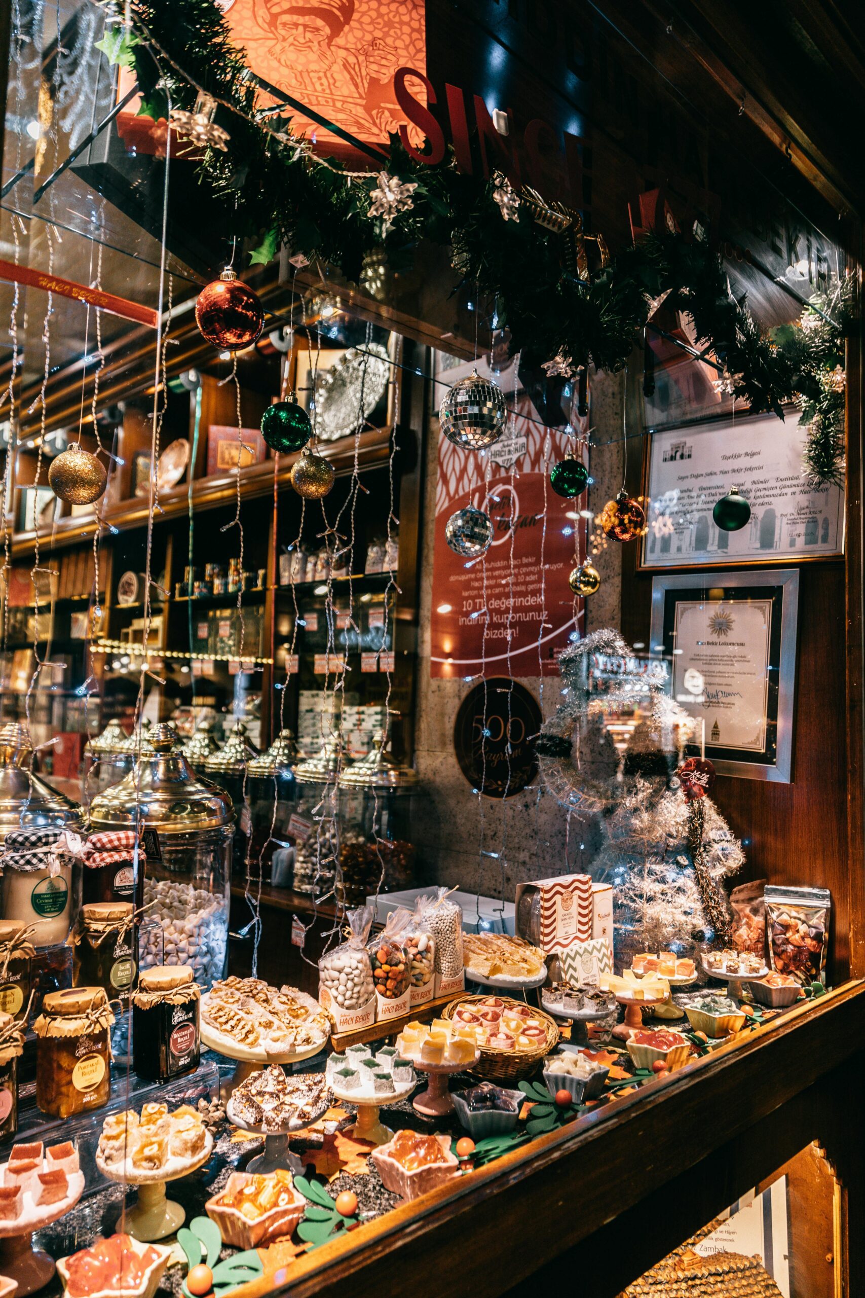 Festive holiday storefront display with Christmas lights, ornaments, and assorted sweets including Turkish delights and preserves